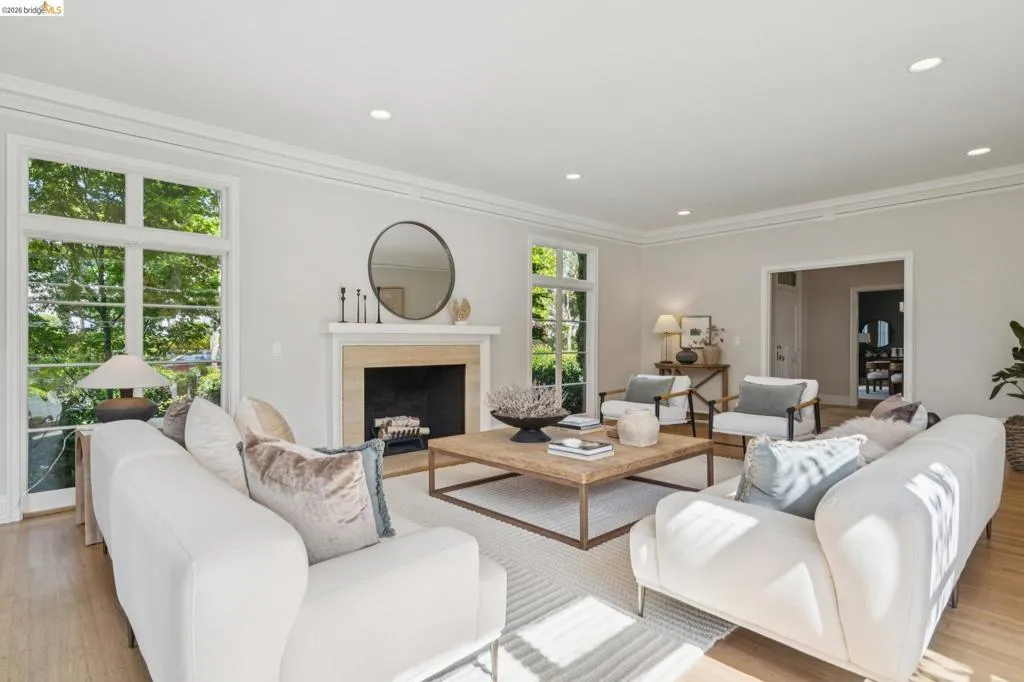 Living room featuring a fireplace with a light-toned surround, recessed lighting, crown molding, wood-finish flooring, and multiple large windows
