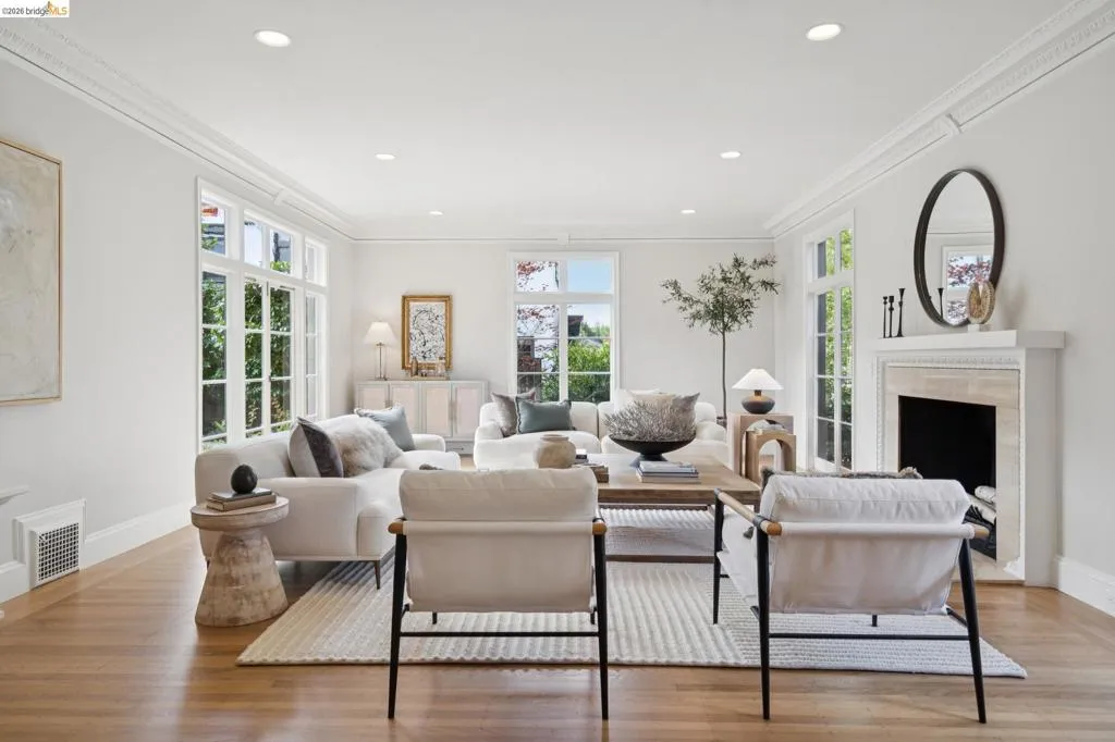 Spacious living area featuring wood-finish flooring, abundant natural light from multiple large windows, recessed ceiling lighting, and detailed crown molding