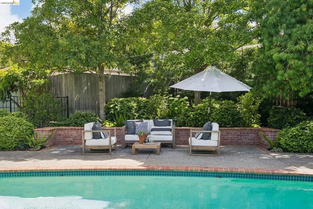 Inviting poolside patio featuring a brick retaining wall and mature perimeter landscaping