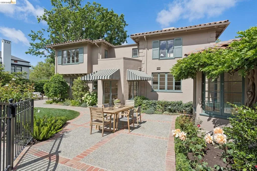 Exterior stucco residence with a red tile roof, featuring multiple windows with light blue shutters and a striped awning over an entry