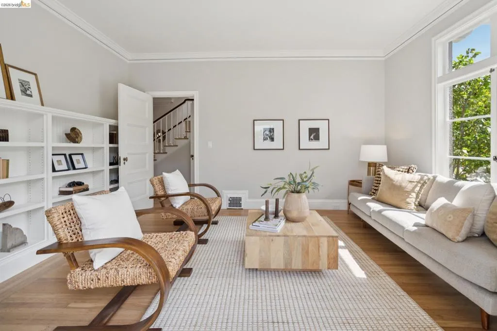 Living area featuring wood-finish flooring, built-in shelving, crown molding, and large windows