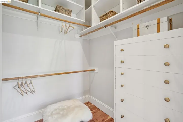 Walk-in closet featuring built-in white shelving, multiple hanging rods, a white built-in dresser with brass-finish knobs, and cedar flooring.