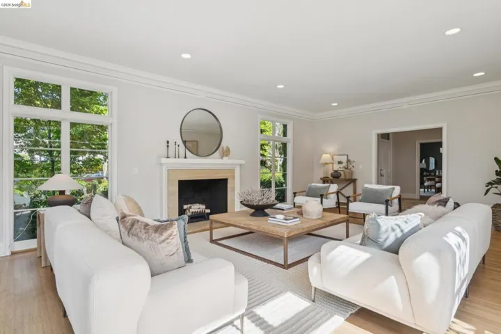 Living room featuring a fireplace with a light-toned surround, recessed lighting, crown molding, wood-finish flooring, and multiple large windows