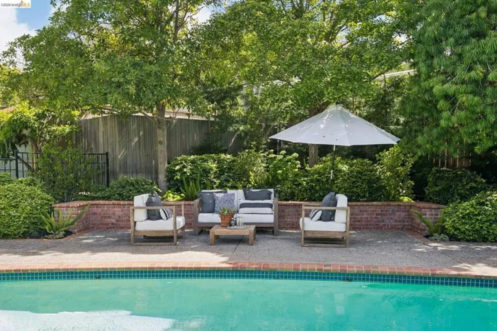 Inviting poolside patio featuring a brick retaining wall and mature perimeter landscaping