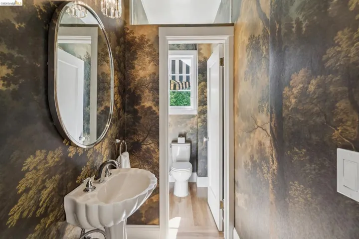 Powder room featuring a pedestal sink with a decorative shell-edged basin, a polished chrome faucet, an oval wall-mounted mirror, and an overhead crystal light fixture