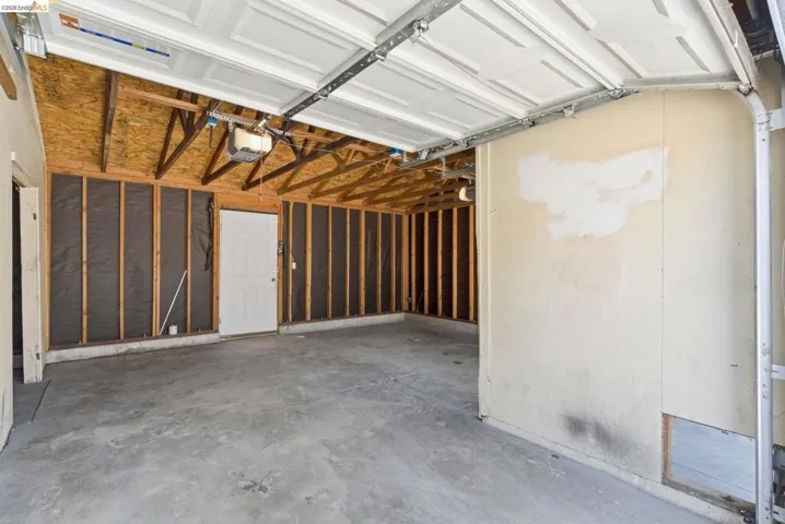 Garage interior featuring a concrete floor, exposed wood framing, and an overhead garage door mechanism