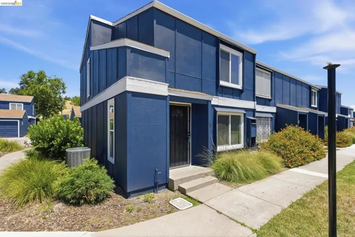 Exterior townhouse featuring a deep blue facade with white trim, a concrete walkway, mature landscaping, and an entry door with security screen