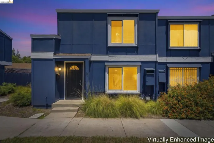 Blue exterior facade with white trim, featuring a dark entry door with an arched window insert and a porch light fixture