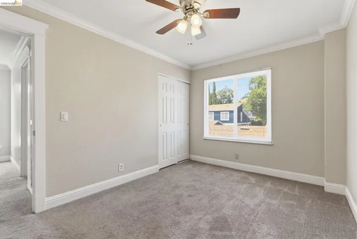 Carpeted room featuring a ceiling fan, white trim, a double-pane window with blinds, and bi-fold closet doors