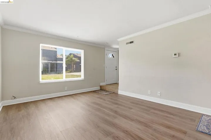 Spacious living area featuring wood-finish flooring, neutral wall tones, white trim, and a large window