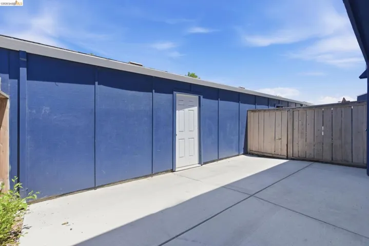 Spacious concrete patio area featuring a privacy fence and direct exterior access via a white paneled door