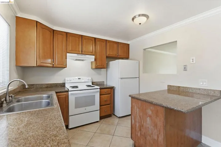 Kitchen featuring wood cabinetry, solid surface countertops, a double basin sink, white electric range with overhead vent, and tile flooring