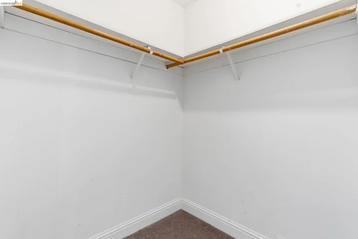 Corner closet with white walls, two wooden hanging rods, and an upper shelf