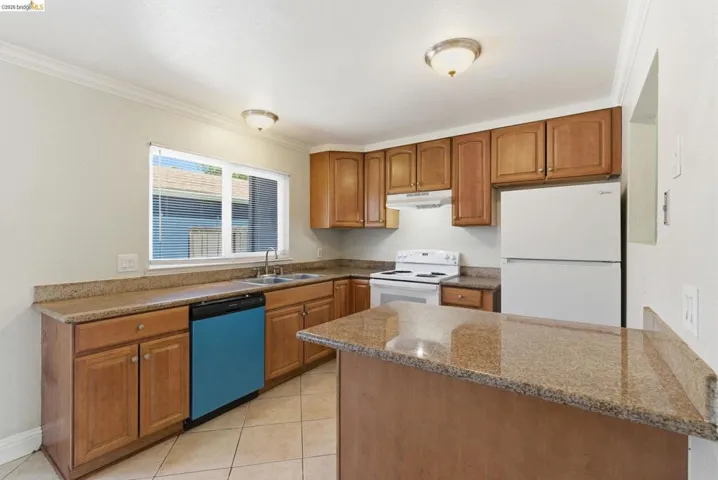 Kitchen featuring wood cabinetry, light-toned countertops, a stainless steel sink, and white appliances