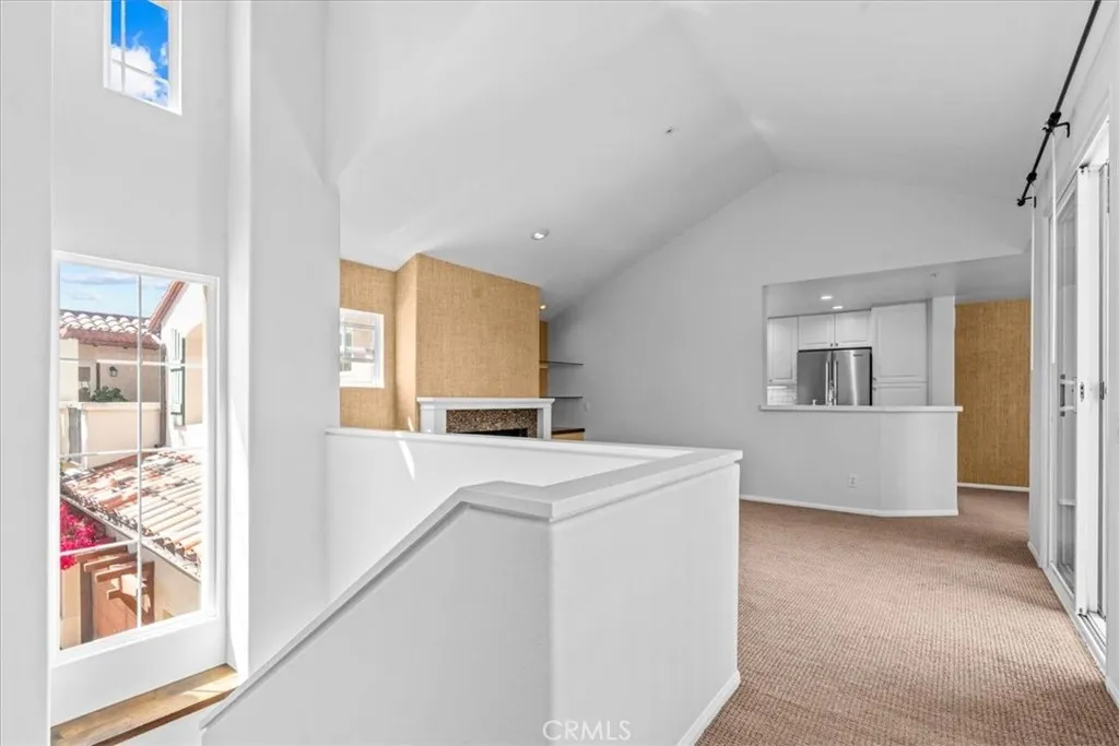 View from top of stairs looking toward living room with vaulted ceiling and kitchen