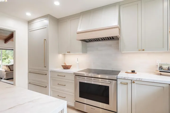 Gourmet kitchen featuring a paneled refrigerator, integrated stainless steel range, custom range hood, subway tile backsplash, and stone countertops