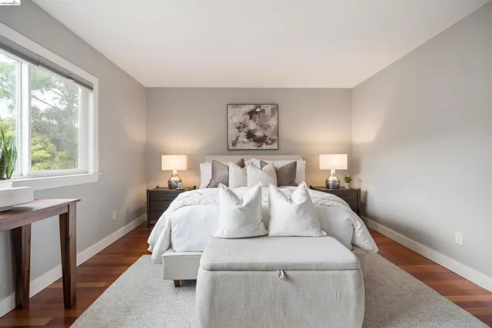 Recessed lighting illuminates a space featuring wood-finish flooring, a large window, and light gray wall paint
