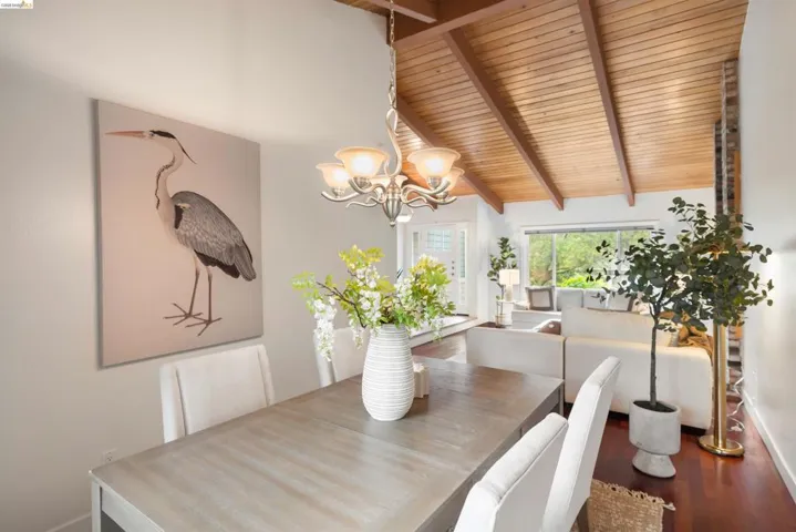 Open-concept room featuring a vaulted wood-paneled ceiling with exposed beams, dark wood-finish flooring, and a contemporary chandelier