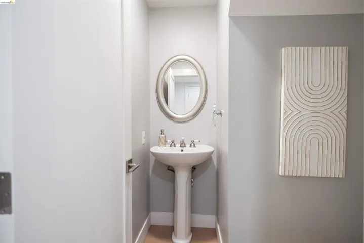 Pedestal sink with a polished chrome faucet, an oval wall mirror, light gray wall paint, and wood-finish flooring