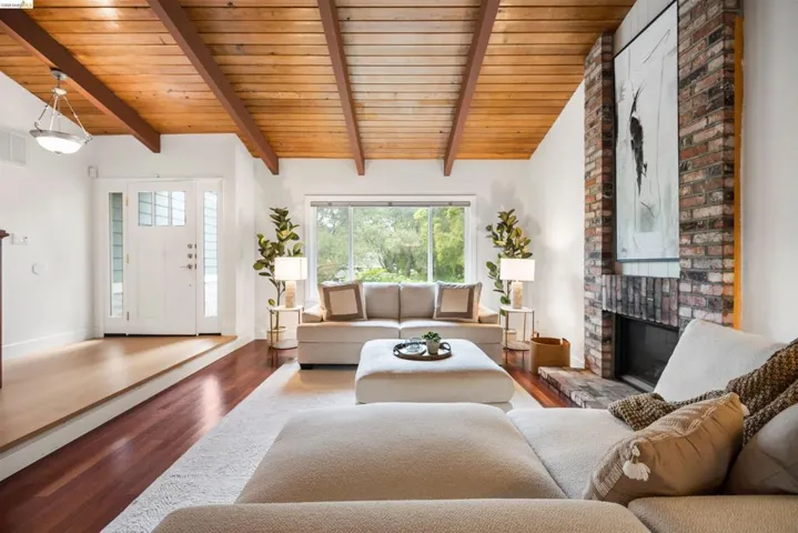 Living area featuring a floor-to-ceiling brick fireplace, wood-finish flooring, and a vaulted ceiling with exposed wood beams