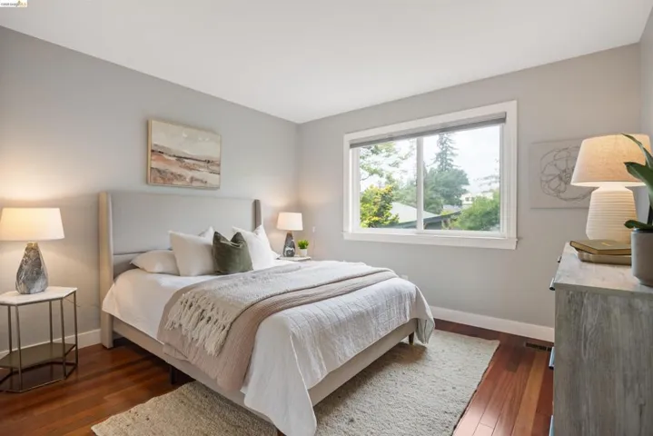 Bright bedroom featuring wide plank wood-finish flooring and a large window with white trim