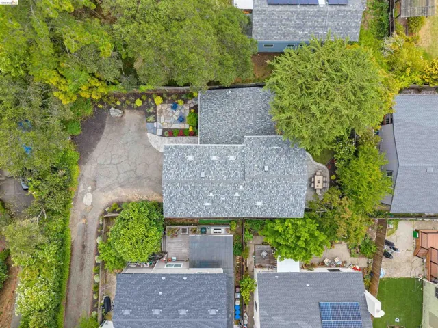 Aerial perspective showcasing a property with a grey shingle roof, a stone patio, and a paved driveway