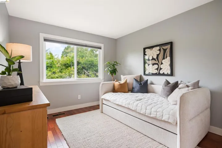 Hardwood flooring with a soft area rug, a large window with white trim, and light gray wall paint