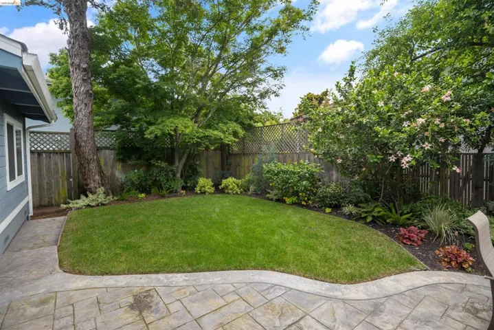 Private backyard featuring a stamped concrete patio, a central lawn area, and mature perimeter landscaping with varied foliage