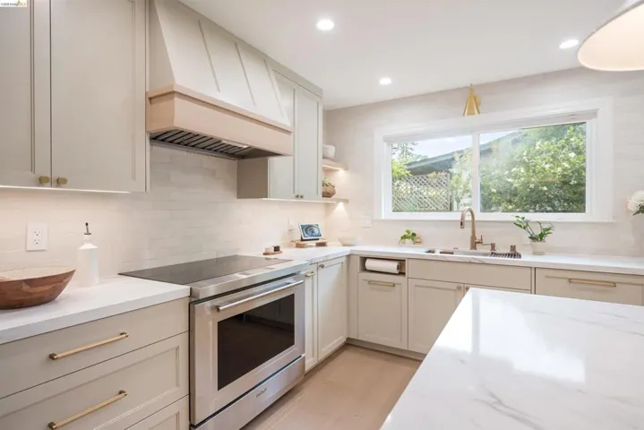 Kitchen featuring light wood-finish flooring, white countertops, and light-colored cabinetry with brass hardware