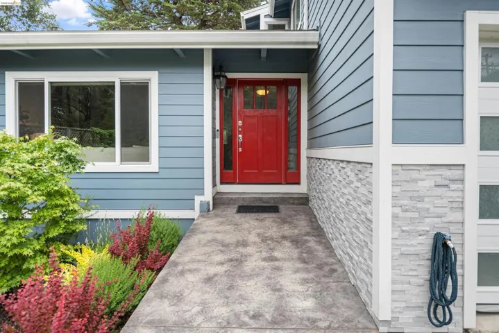Welcoming entry with a vibrant red door, complementary blue siding, stacked stone accents, a concrete walkway, and established landscaping