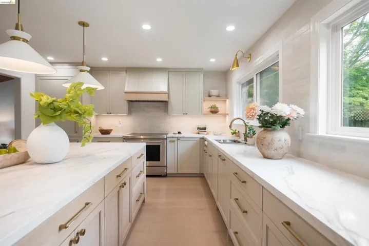 Bright kitchen featuring a central island with a stone-finish countertop, light wood-finish flooring, recessed lighting, double pendant lights, and stainless steel appliances