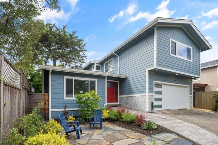 Contemporary blue siding exterior featuring a red entry door, an integrated garage with a modern door design, a flagstone patio, and mature landscaping