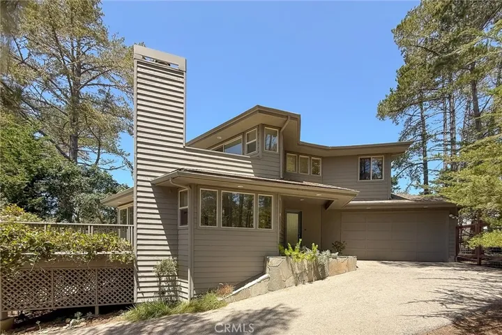 The driveway approach showcases the home’s custom architecture, wooded setting, and attached two-car garage.