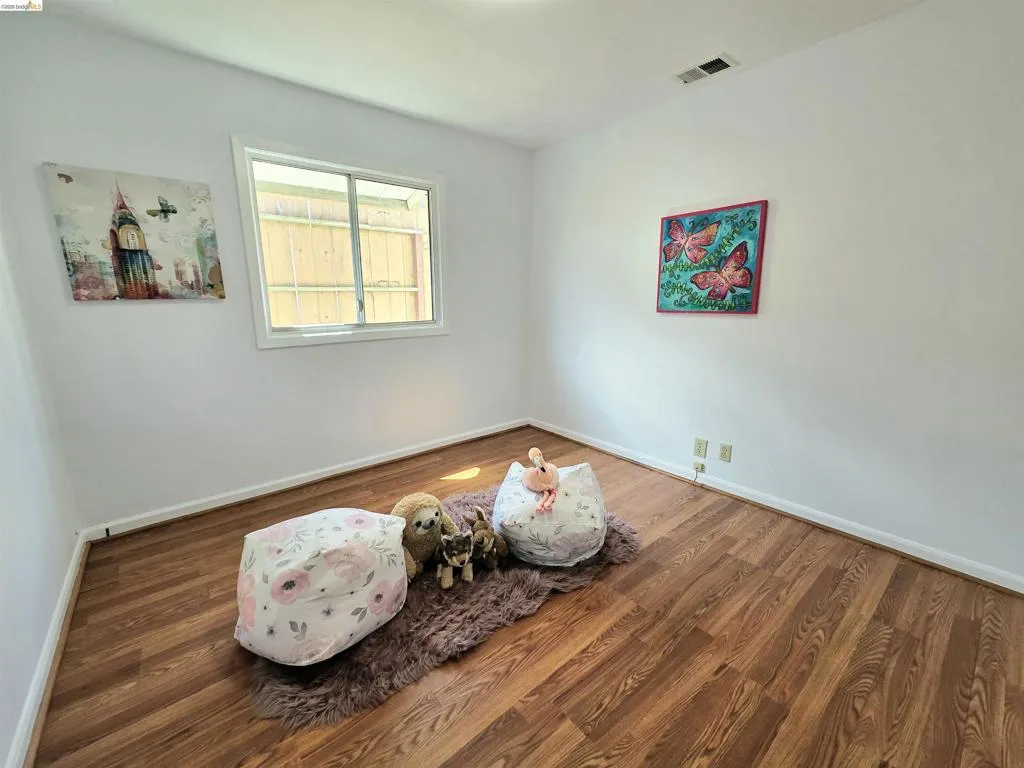 Bright interior room featuring wood-finish flooring, white walls, and a white trim baseboard