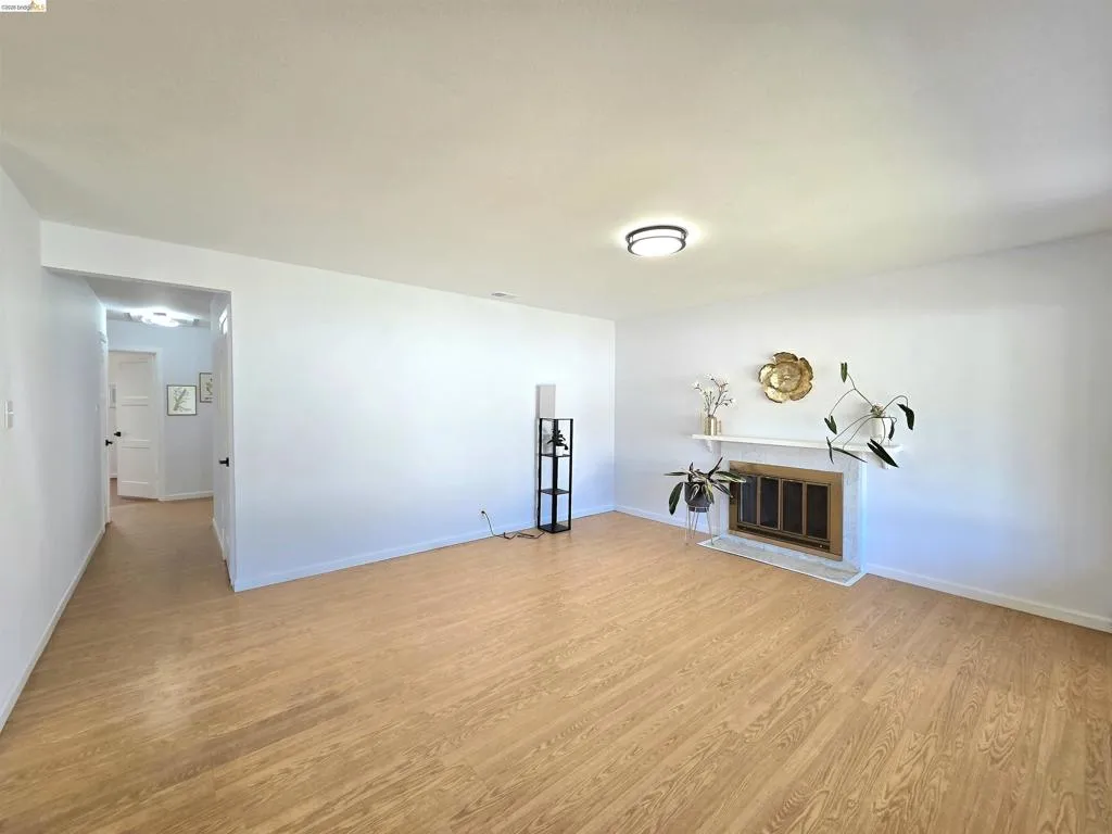 Bright living area featuring wood-finish flooring, a white mantel, and a fireplace with a brass-toned screen