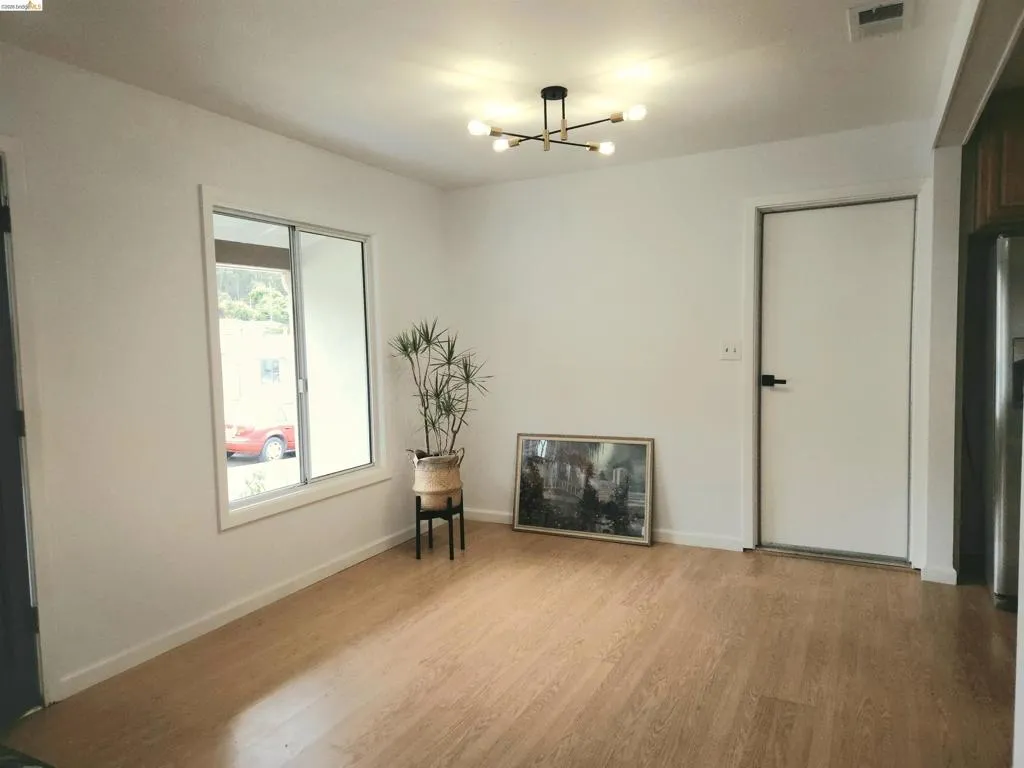 Bright interior space featuring light wood-finish flooring, a modern multi-bulb ceiling fixture, a sliding window, and crisp white walls