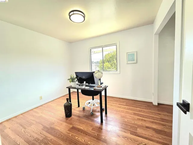 Spacious room featuring wood-finish flooring, a window with exterior views, white walls, and a modern ceiling light fixture