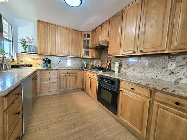 Kitchen featuring ample wood cabinetry, granite countertops, a built-in stainless steel sink, and wood-finish flooring