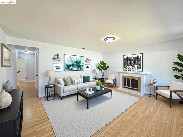 Spacious living area featuring wood-finish flooring, a white mantel fireplace with a gold-tone insert, and light-toned walls. Virtual staging.