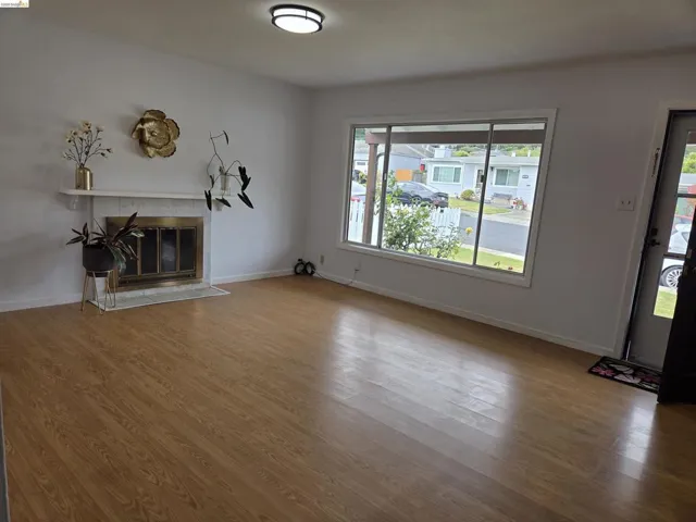 Spacious living area featuring wood-finish flooring, a white mantel fireplace with a brass firebox, and a large picture window