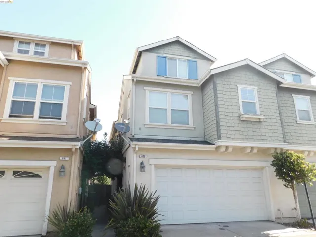 Contemporary multi-level residence featuring a two-car garage, varied exterior siding including stucco and shingle accents, multiple windows with white trim, and a dormer with blue louvered shutters