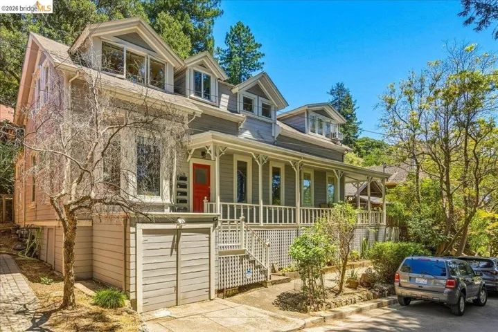 Gray siding exterior featuring a red entry door, white porch railing, and dormer windows
