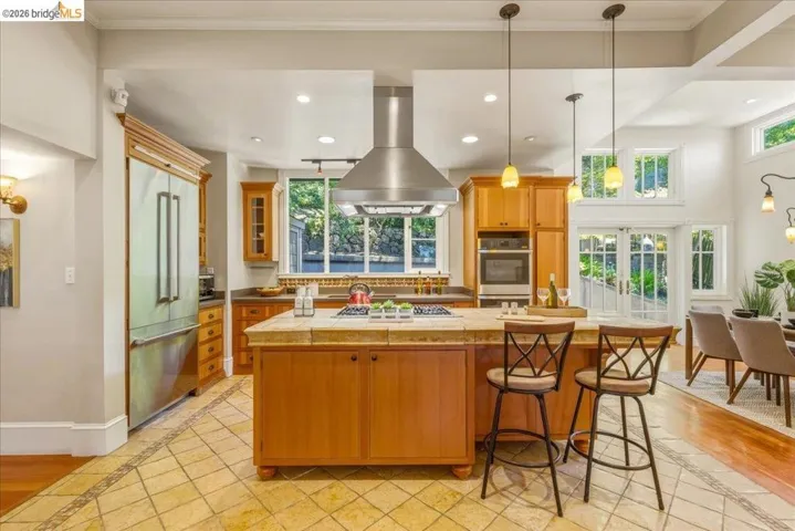 Spacious kitchen featuring an island with counter seating, stainless steel appliances, wood cabinetry, and tile flooring