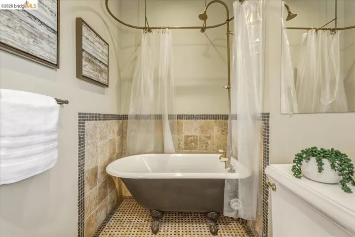 Clawfoot bathtub with an overhead shower fixture, complemented by natural stone tile wainscoting and mosaic accents
