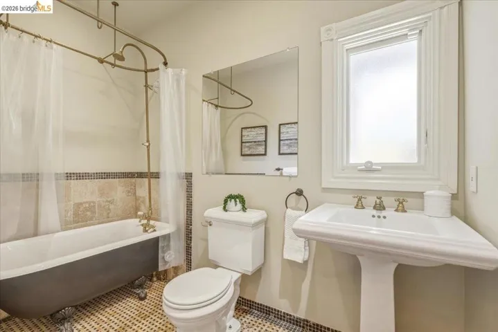 Vintage-inspired bathroom featuring a clawfoot tub with an overhead shower fixture, a classic pedestal sink, and a framed window with frosted glass