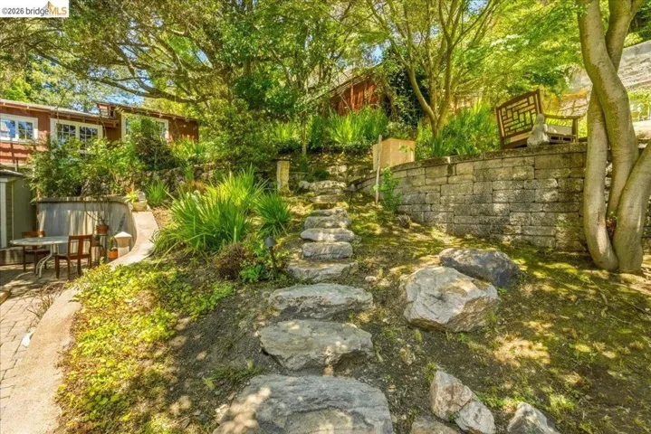 Stone pathway ascending a landscaped hillside featuring mature trees and established greenery