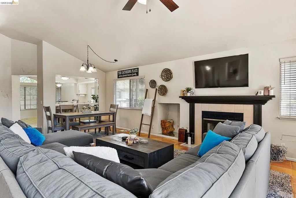 Living area featuring ceiling fan, plenty of natural light, vaulted ceiling, a fireplace, and a chandelier
