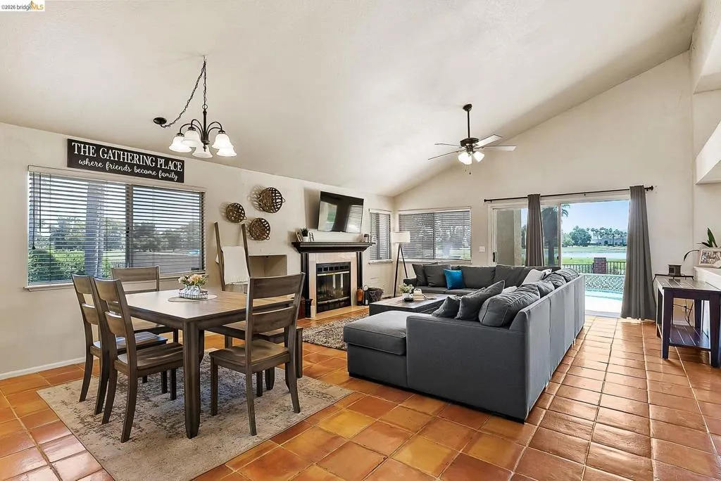Dining space featuring light tile patterned flooring, a ceiling fan, a chandelier, a tiled fireplace, and high vaulted ceiling