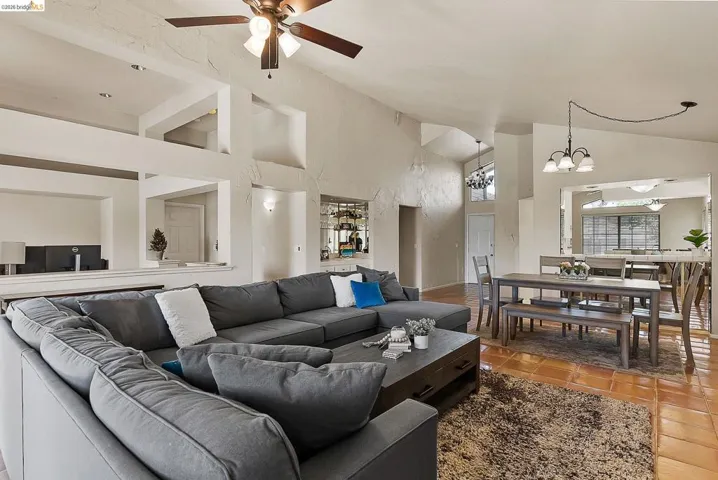 Living room featuring a ceiling fan, high vaulted ceiling, a chandelier, and tile patterned floors