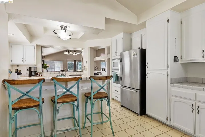 Kitchen with white cabinets, white appliances, a kitchen bar, vaulted ceiling, and light tile patterned floors